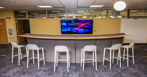 six high top chairs and a bar-like table are arranged in front of a big screen TV